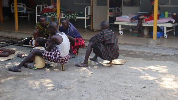 Eight-year-old Esekon Nangiro sits on the ground with his father, Nangiro Leyopo, outside LCRH treatment facility.