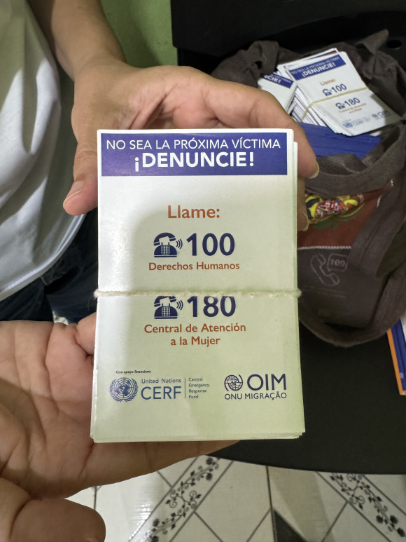 Mayra Figueiras, founder of Humanidade Mais que Fronteiras, shares a pile of cards she plans to distribute with volunteers. "100" is the human rights hotline that can be called to report human trafficking. 