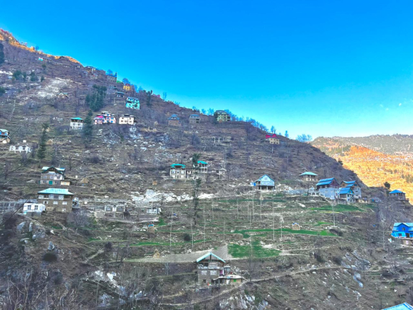 A view of the village of Dhadkai, nestled in the mountains of the Doda district of Jammu and Kashmir, against a blue sky.