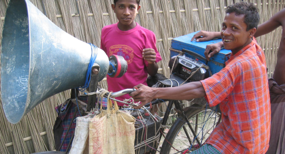 A "mike-ing" man in Gaibandha district, Bangladesh. His job is to ride around to the area villages and spread news of doctors coming to the nearby market, lost children, and new movies playing in town. 