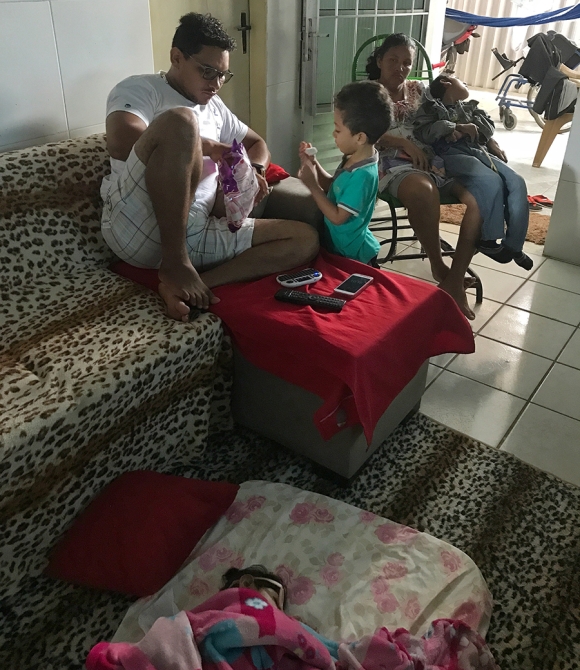 Jorge watches cartoons and eats marshmallows with his stepfather, Luiz Carlos Ribeiro Valadares Junior, while Valentina naps on a mattress near him 