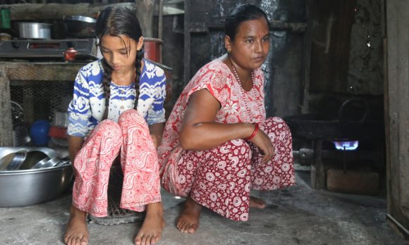 Saraswoti and her mother in their home, surrounded by cooking pots on the floor.