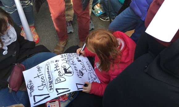 With the crowd looming above, a Connecticut girl takes a moment to add to her protest sign. (Image: Joanne Cavanaugh Simpson)