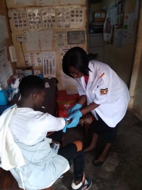 A gloved health worker draws blood from a seated client.