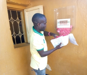 Health worker wearing a pale yellow polo shirt displays a condom dispenser.