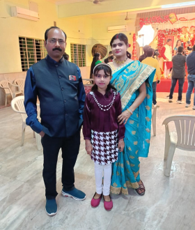 Adrija Mudi, center, wearing a maroon top and a maroon and white plaid skirt, with her father (left) wearing a blue button down shirt and jeans, and her mother (right) wearing a turquoise and gold sari.